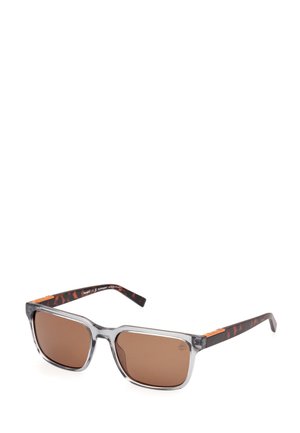 Gafas de sol transparentes grises con lentes marrones, que presentan un patrón de carey en las patillas. Tienen forma cuadrada y detalles metálicos.