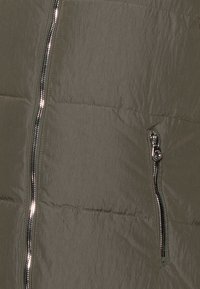 Donkergroene gewatteerde jas in een close-up, met een glanzende rits en gewatteerde textuur. Lichtgewicht materiaal met een gladde afwerking.