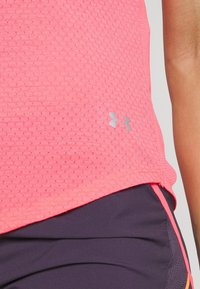 Camisa atlética texturizada de color rosa con dobladillo redondeado y logo plateado. Combinada con pantalones cortos morados oscuros con acentos naranjas y un acabado suave.