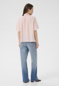 Haut en tissu froncé rose avec des manches courtes et un col volanté, associé à un jean taille haute bleu clair et des chaussures marron.