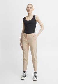 Černé žebrované tílko spárované se světle růžovými střihovými kalhotami a černými vysokými teniskami, vytvářející moderní casual outfit.