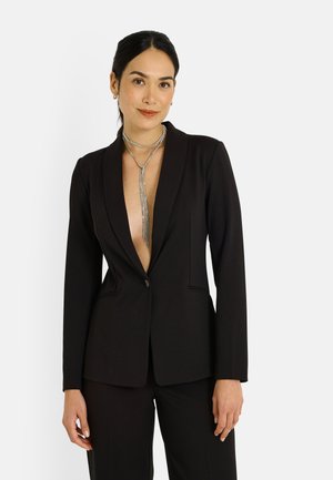 Blazer negro a medida con un escote en V profundo, cierre de un solo botón y solapas marcadas. Tela lisa con un corte estructurado y bolsillos laterales.