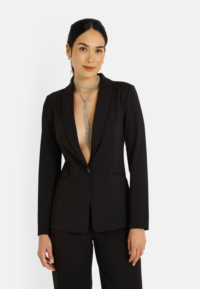 Blazer noir ajusté avec un profond décolleté en V, fermeture à un bouton et revers nets. Tissu lisse avec une coupe structurée et poches latérales.