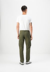 Men's olive green cargo pants with multiple side pockets, a fitted design, and back patch pockets, paired with a plain white t-shirt.