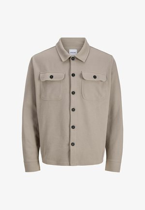 Veste chemise beige clair en tissu texturé, dotée d'un col, de deux poches poitrine et de fermetures à boutons noirs.