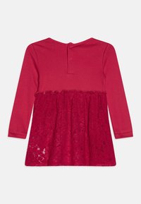 Vestido rojo de manga larga con una parte superior lisa y una falda inferior de encaje, con un dobladillo con volantes y cierre de botones en la parte trasera.