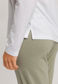 Camisa blanca de manga larga con aberturas laterales, combinada con pantalones ajustados de color verde claro. La camisa está confeccionada con un suave material de algodón texturizado.