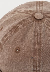 Καφέ υφαντό καπέλο μπέιζμπολ με ραμμένες τρύπες αερισμού και κουμπί επενδυμένο με ύφασμα στην κορυφή.