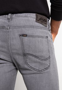 Gray denim jeans featuring a back pocket with contrasting stitching and a leather label with the brand "Lee" at the waistband.