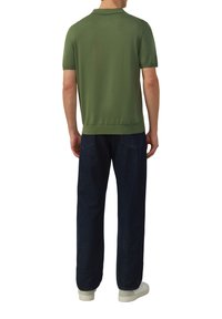 Koszula polo z krótkim rękawem w ciemnozielonym kolorze, wykonana z bawełny, z kołnierzykiem, ściągaczem na dole, zestawiona z luźnymi ciemnoniebieskimi dżinsami i białymi butami.