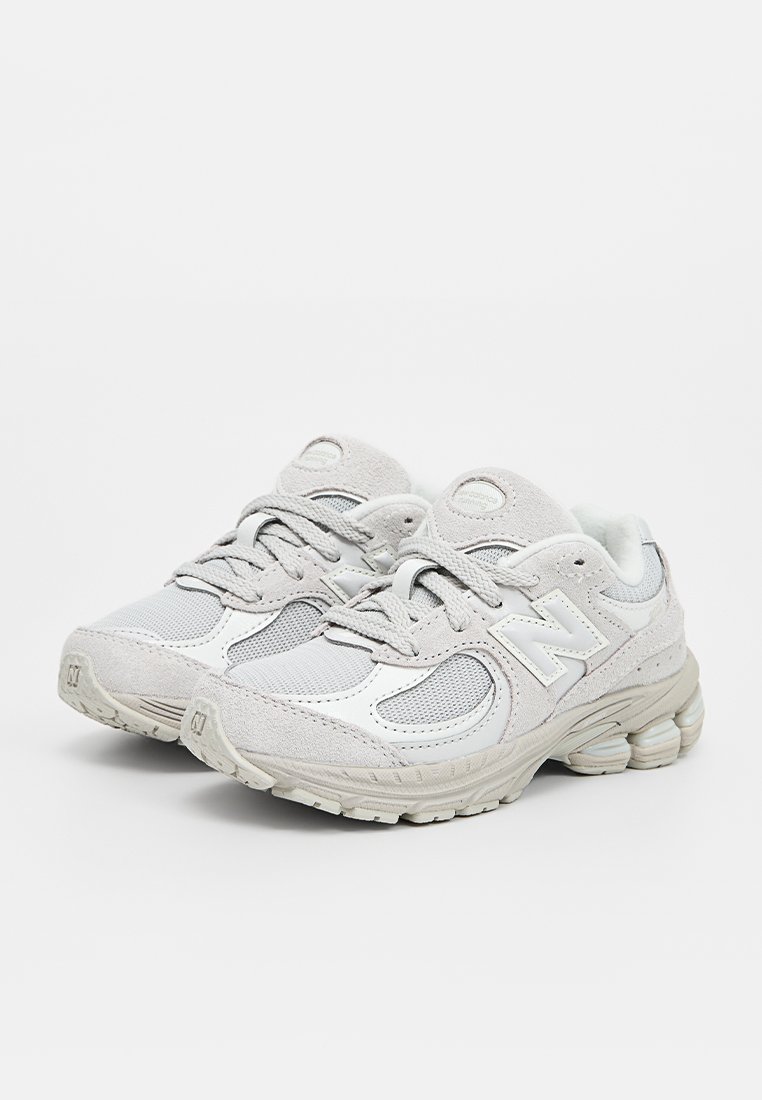 Zapatillas deportivas de color gris claro que combinan materiales de malla y ante, con suelas acolchadas y un detalle de logo prominente en los laterales.