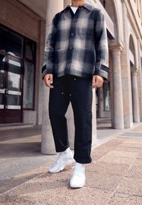 Giacca a quadri in bianco e nero con chiusura a bottoni, pantaloni neri e sneakers bianche. Tessuto liscio e vestibilità casual; i pantaloni hanno dettagli dorati.