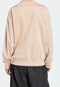 Světle béžový svetr s dlouhým rukávem vyrobený z hladkého materiálu, má vysoký límec a elastický lem, v kombinaci s volně střiženými tmavými kalhotami.