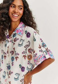 Košile s krátkými rukávy z lehkého materiálu s bílým základem. Obsahuje barevné květinové a paisley vzory, vzorovaný límec a knoflíky.