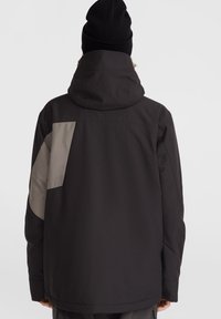Chaqueta negra con capucha, que presenta un acento gris en la parte posterior y las mangas. Hecha de un material suave y duradero con un corte relajado.