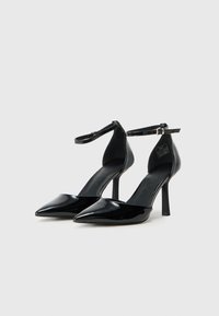 Crne lakirane visoke potpetice s izduženim prstima, remenima oko gležnjeva i uskim stiletto potpeticama. Glatka tekstura s sjajnim finišom.