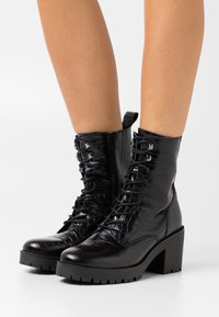 Bottines noires à lacets avec une texture embossée effet croco, dotées d'un talon épais, d'une fermeture éclair latérale et d'une semelle robuste.