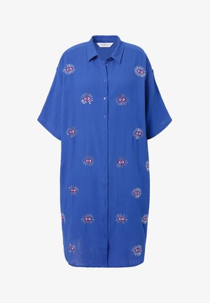Modrá košile s krátkým rukávem, zdobená vyšívanými motivy očí obklopenými slunečními vzory v kontrastních barvách.