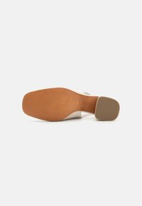 Chaussure à talon blanche avec un orteil carré, dotée d'une tige lisse et d'une semelle en bois brun contrastant avec un talon texturé pour une meilleure adhérence.
