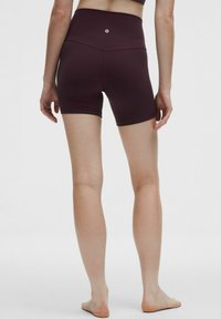 Pantalones cortos deportivos de talle alto en burdeos, fabricados con material elástico, que cuentan con una textura suave, una longitud corta y un pequeño logo en la parte trasera.