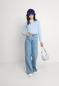 Top lungo a maniche, blu chiaro, con un design sottile, jeans wide-leg in denim chiaro a vita alta, scarpe bianche e una borsa morbida blu.