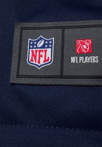 Marineblauer Stoff mit einem NFL-Logo-Patch; verfügt über einen grauen Hintergrund und rote Akzente. Zeigt "NFL PLAYERS" in weißem Text unter dem Logo.