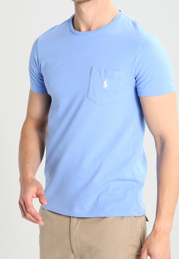 Světle modré bavlněné tričko s krátkými rukávy, kulatým výstřihem a kapsou na hrudi, která má malé vyšívané logo.