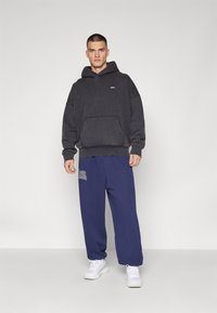 Σκούρο γκρίζο φούτερ με μπροστινή τσέπη και μικρό λογότυπο, σε συνδυασμό με χαλαρές ναυτικές φόρμες που έχουν λευκή επιγραφή, ολοκληρωμένο με λευκά αθλητικά παπούτσια.