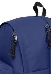 Zaino in tessuto blu con una parte superiore arrotondata, dotato di cerniere nere e lacci su entrambi i lati. Texture liscia, materiale resistente.