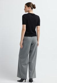 Top noir à manches courtes avec une texture scintillante, associé à un pantalon large taille haute gris et des escarpins noirs pointus.