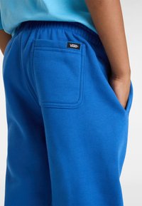 Blauwe trainingsbroek van zacht materiaal met een elastische tailleband. Heeft een enkele achterzak met een zwart Vans logo label.