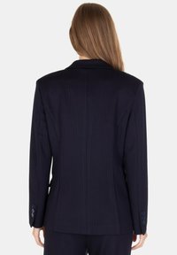 Blazer a righe sottili blu navy, taglio sartoriale, spalle strutturate, spacco singolo sul retro, polsini con quattro bottoni e tessuto dalla trama liscia.