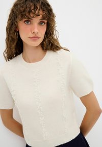 Kurzarmpullover aus Creme mit einem strukturierten Muster, das vertikal verläuft. Hergestellt aus weichem Material, mit einem Rundhalsausschnitt und schmaler Silhouette.
