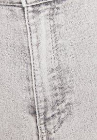 Ljust grå denimtyg med en strukturerad yta, med synliga sömmar och ett subtilt bleknat mönster. Närbild av en fickområde.