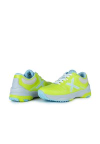 Zapatillas deportivas de color amarillo brillante con acentos en azul claro, parte superior de malla, suela texturizada y cordones blancos. Presenta un logo prominente en azul claro.