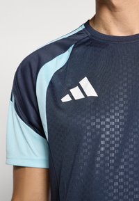 Navy blue athletic shirt with light blue accents. Features a textured pattern and white Adidas logo on the chest. Short sleeves, round neckline.