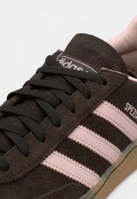 Καφέ σουέντ αθλητικό παπούτσι με μαύρα κορδόνια, ροζ ριγέ με υφή και λευκό λογότυπο. Διαθέτει καουτσούκ σόλα με στρογγυλεμένη σχεδίαση στη μυτούλα.