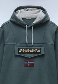 Donkergroene hoodie met een grijze binnenvoering. Beschikt over een grote voorpatch met de tekst "NAPAPIJRI geographic" en een rood Noors vlagembleem.