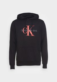 Sudadera negra de mezcla de algodón, con un gran logo rojo "CK" y texto "CALVIN KLEIN JEANS". Incluye un bolsillo delantero y capucha con cordón.