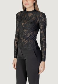 Top nero a maniche lunghe con sovrapposizione in pizzo floreale, forma aderente, colletto alto e motivo testurizzato, abbinato a pantaloni neri.