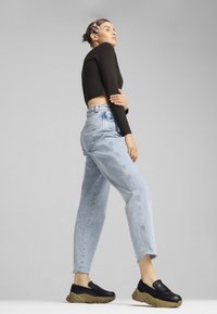 Top negru scurt cu mânecă lungă, blugi ușor albaștri cu talie înaltă și croială dreaptă, și pantofi negri slip-on cu sole chunky bej. Accesorii simple pentru păr.