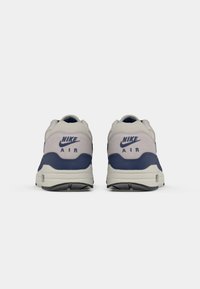 Nike Air spordijalatsitel on hall ja mereväe sinine ülemine osa, tekstureeritud kangaga, pehmendatud tald ja nähtav õhuüksus. Bränding kandadel.