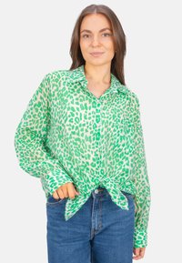 Green leopard print shirt with a button-up design and knotted hem. Made of lightweight fabric with a collared neckline and long sleeves.