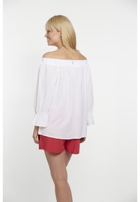 Weiße schulterfreie Bluse mit elastischem Ausschnitt, langen Puffärmeln und Raffung, kombiniert mit roten Shorts.