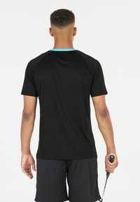 Svart idrottströja med blå halsringning, korta raglanärmar och slät textur, ihopparad med svarta shorts och ett tennisracket.