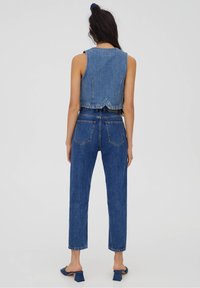 Modrý denimový vest a džínové kalhoty s vysokým pasem. Vest má zkrácený střih a rozparek na zadní straně; kalhoty mají rovné nohavice a tradiční kapsy.