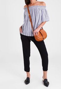 Paskowana bluzka typu off-the-shoulder, czarne zwężane spodnie i czarne klapki. Brązowa torebka na ramię z detalem w postaci klamry. Gładkie materiały i dopasowany krój.