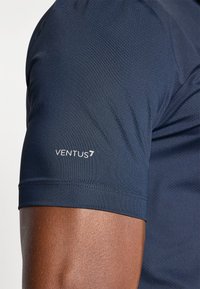 Μπλουζάκι με κοντά μανίκια σε ναυτικό χρώμα, κατασκευασμένο από υλικό με υφή και αναπνεύσιμες ιδιότητες. Διαθέτει το λογότυπο "VENTUS7" σε λευκό χρώμα στο αριστερό μανίκι.