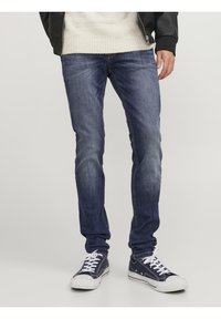 Jeans in denim di colore blu scuro con una texture sbiadita, slim fit e dettagli di cucitura. Abbinati a sneakers navy con lacci e suole bianche.