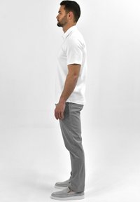 Witte polo, grijze broek en grijze instappers. Casual fit, korte mouwen, soepel materiaal, zijaanzicht tegen een effen achtergrond.